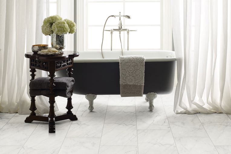 bright bathroom remodel with stone tile floors and a free standing tub near a bright window with sheer white drapes